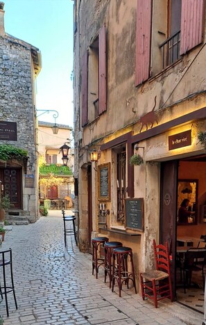 A cobblestone street with outdoor seating, stone buildings, and a café with a sign reading 'le chat vire'. - Apartment in the heart of a medieval village with a view of the sea (Tourrettes-sur-Loup)