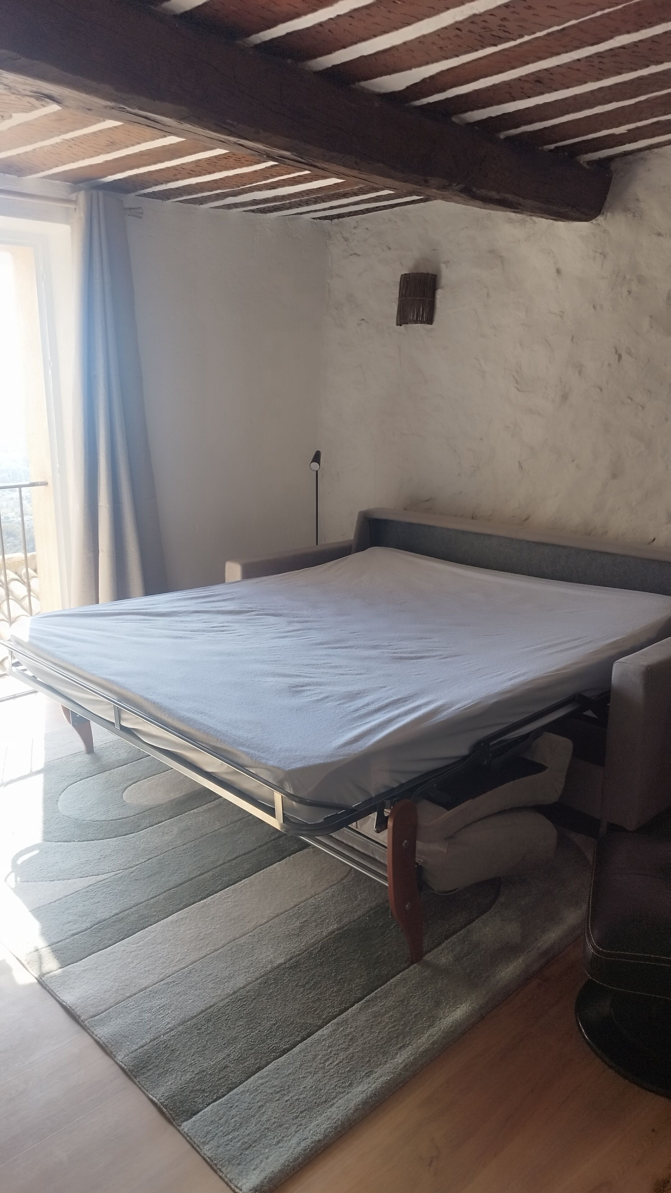 Ein Zimmer mit einem Bett, einem kleinen Tisch und einem Fenster mit Vorhängen.