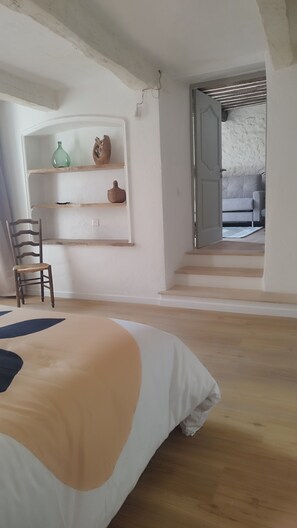 A bedroom with a bed, a chair, a shelf with decorative items, and a staircase leading to another room. - Apartment in the heart of the medieval village with a view of the sea   (Tourrettes-sur-Loup)