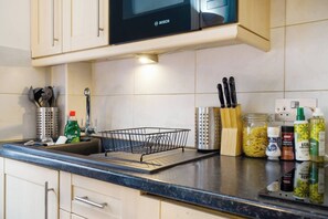 A kitchen with a Bosch microwave, a sink with a dish rack, and various kitchen utensils and condiments. - Cozy Studio in the Heart of the City of London B (London)