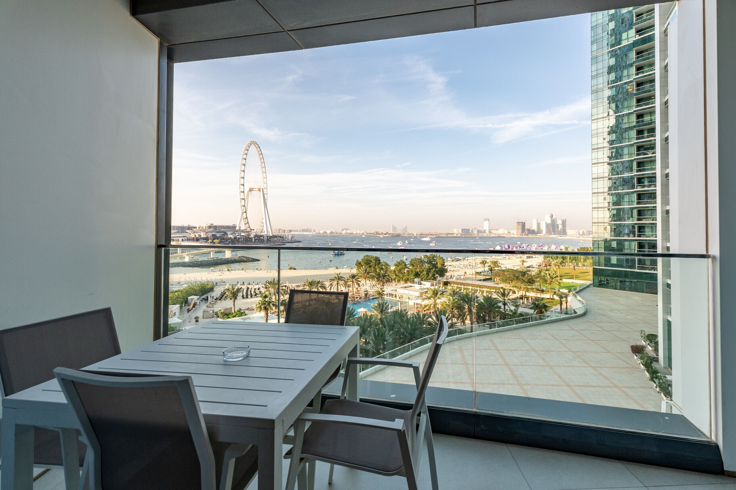 Un balcon avec vue sur une grande roue, une plage et un bâtiment moderne.