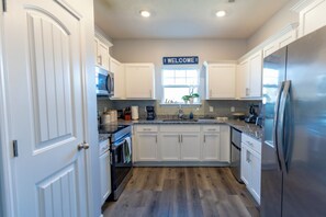 A modern kitchen with white cabinetry, a stainless steel refrigerator, and a welcome sign above the sink.