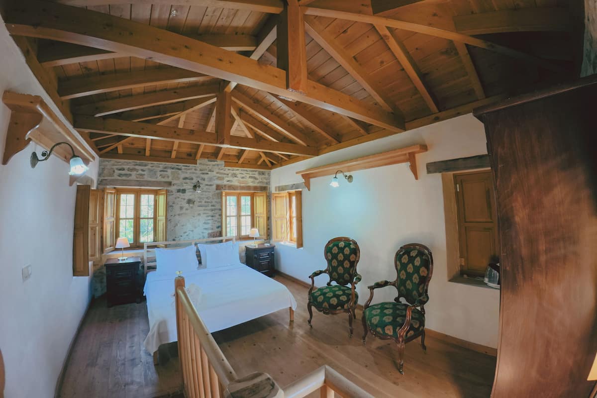 Ein Schlafzimmer mit Holzboden, Steinwänden, einem Bett, zwei Stühlen und einem kleinen Tisch.