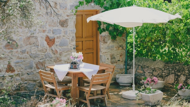 Un muro in pietra con una porta di legno, un tavolo con sedie e un ombrellone bianco.
