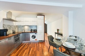 Une cuisine compacte dotée d’appareils électroménagers modernes, un coin repas avec une table en verre et un lave-linge visible.