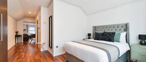 Ein Schlafzimmer mit einem großen Bett, einem Nachttisch und einem grünen Schrank. Im Hintergrund ist eine Essecke mit Tisch und Stühlen zu sehen.