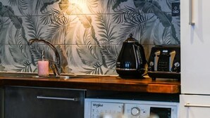 Moderni keittiö, jossa on astianpesukone, kahvinkeitin ja vedenkeitin työtasolla.