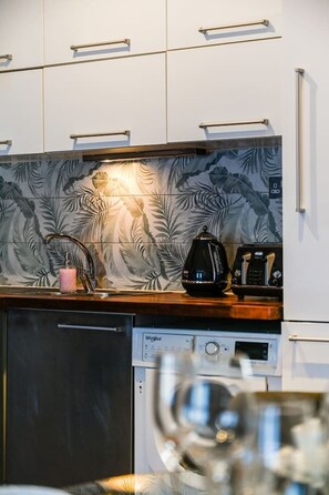A modern kitchen with a dishwasher, a coffee maker, and a kettle on the counter. - Avari - Stylish New 1BR Apartment in Hatton Garden (London)