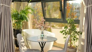 Une pièce baignée de lumière, avec une table ronde, deux chaises, une plante en pot et une baignoire.