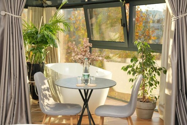 Una habitación iluminada por el sol con una mesa redonda, dos sillas, una planta en maceta y una bañera.