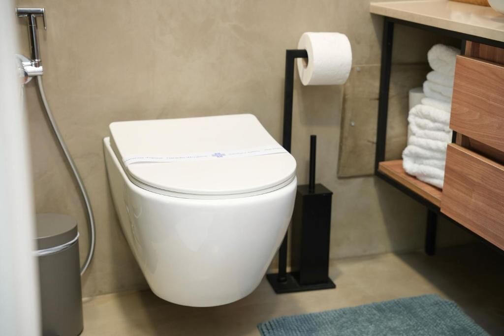 A modern bathroom with a white toilet, a black toilet paper holder, and a towel rack with folded towels.