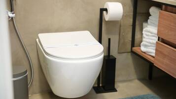 A modern bathroom with a white toilet, a black toilet paper holder, and a towel rack with folded towels.