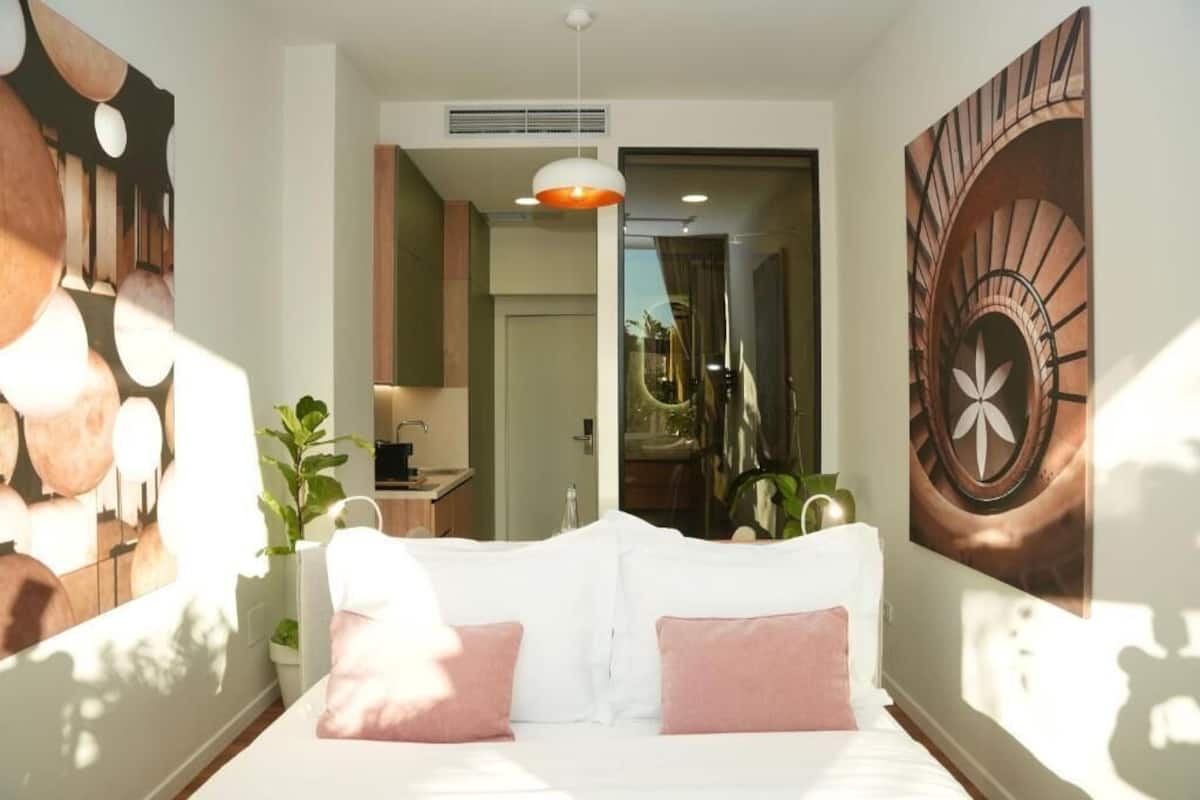 Ein modernes Hotelzimmer mit einem Bett, einer Zimmerpflanze und einem großen Gemälde an der Wand.