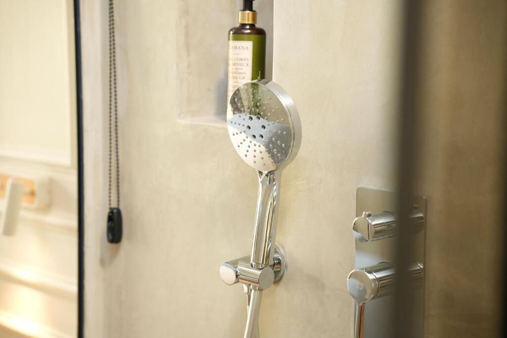 A shower with a handheld showerhead and a bottle of shampoo.