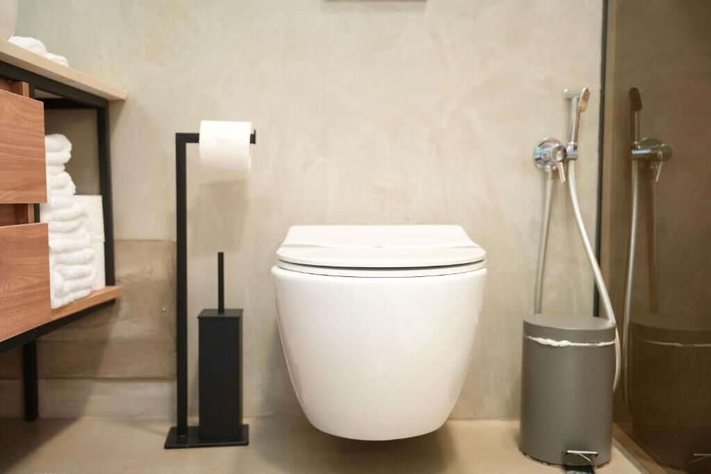 Un baño moderno con inodoro blanco, dispensador de papel higiénico, secador de manos y zona de ducha.