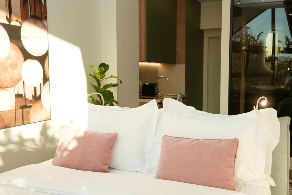 A modern bedroom with a bed, white pillows, and a view of a kitchen area.