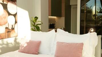 A modern bedroom with a bed, white pillows, and a view of a kitchen area.