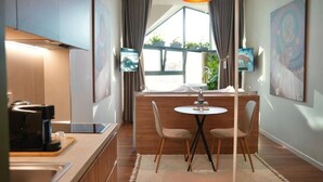Une cuisine moderne équipée d’une machine à café, d’un coin repas avec deux chaises, une petite table et une grande fenêtre avec des rideaux.