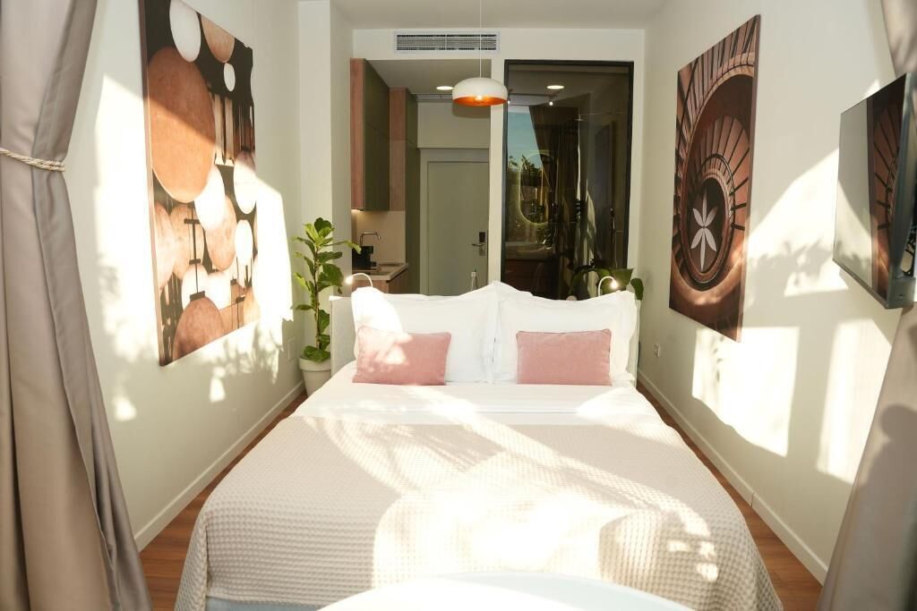 Un dormitorio con una cama grande, una mesita de noche, una planta en maceta y cuadros en las paredes.