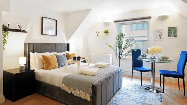 Un dormitorio moderno con cama, mesita de noche y una pequeña zona de comedor con mesa y sillas.