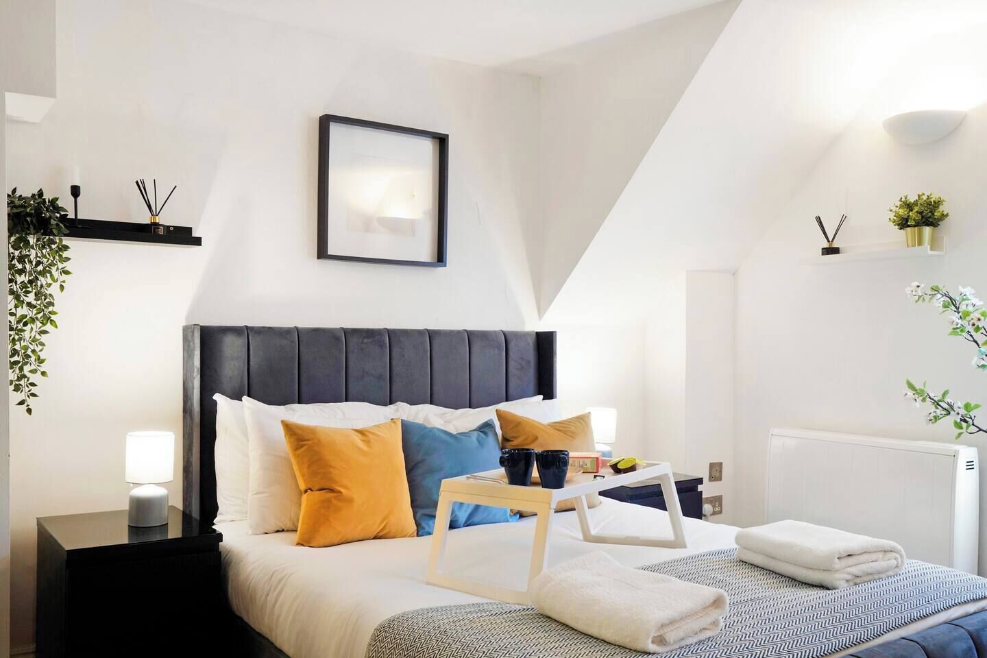 Un dormitorio moderno con cama, mesitas de noche, lámpara de noche, un cuadro enmarco y un radiador.
