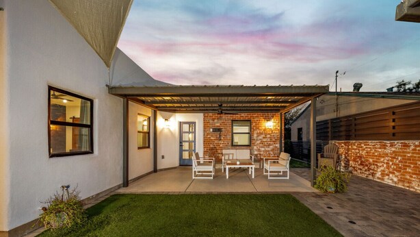 A covered patio with outdoor furniture, a brick wall, and a grassy lawn.