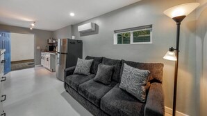 A modern living room with a grey sofa, a floor lamp, and a kitchen area in the background.