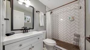 A modern bathroom with a white vanity, a large mirror, a toilet, and a shower area with a herringbone tile pattern.