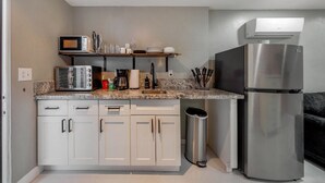 A compact kitchen with white cabinets, a stainless steel refrigerator, a microwave, and a coffee maker on the countertop.