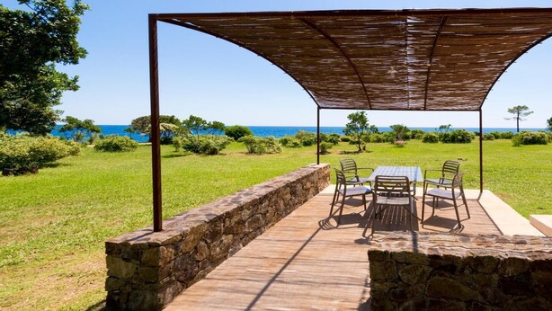 Un patio exterior con una mesa y sillas, un muro de piedra y vistas al mar.
