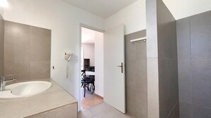 Un baño moderno con una bañera grande, zona de ducha y un inodoro. Se ve una puerta que da a un comedor con una mesa y sillas.