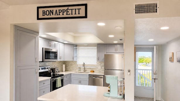 A modern kitchen with grey cabinets, stainless steel appliances, a central island, and a 'BON APPETIT' sign.