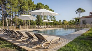 A pool area with lounge chairs and umbrellas, surrounded by a wooden deck and a wooden fence. - Studio 1 living room terrace sea view (Sari-Solenzara)
