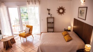 A bedroom with a bed, a chair, a small table, and a nightstand with a lamp. - Studio 1 living room terrace sea view (Sari-Solenzara)