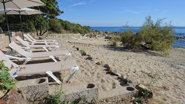 A beach with sun loungers and umbrellas, rocky terrain, and a view of the sea. - Studio 1 living room terrace sea view (Sari-Solenzara)