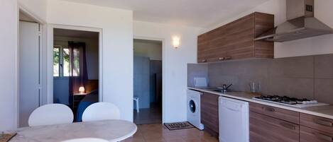 A compact kitchen with a gas stove, washing machine, and wooden cabinets.