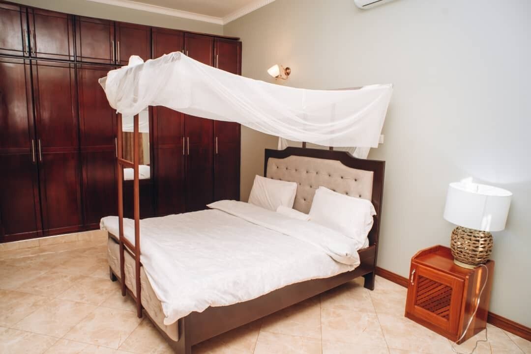 A four-poster bed with a canopy, a tufted headboard, and a bedside lamp.