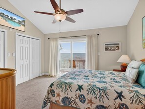 A bedroom with a bed, a ceiling fan, a view of the ocean, and a door to the outside. - Bayfront Kontiki 304 (Rockport)