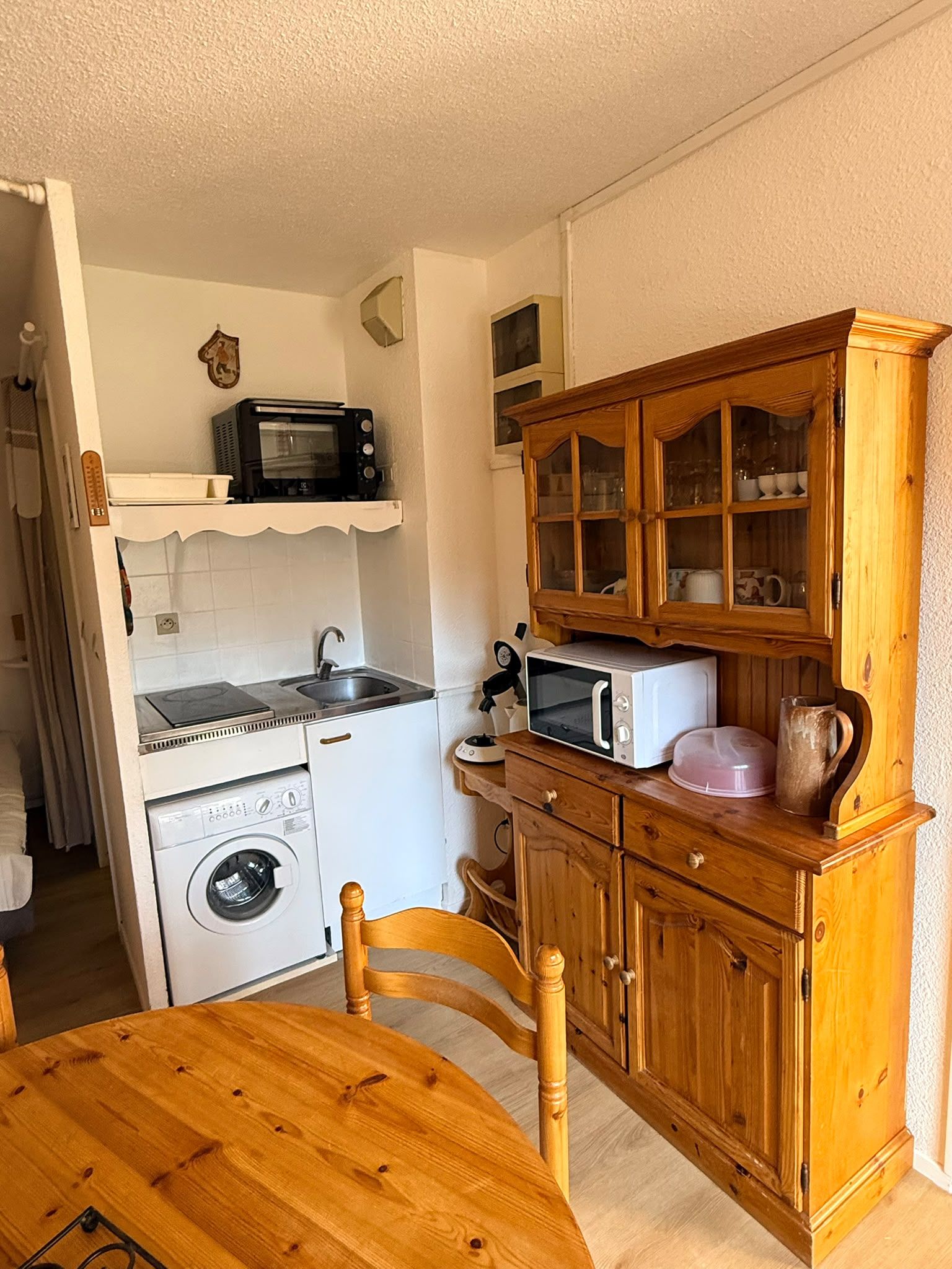 A compact kitchen with a microwave, toaster, and a wooden cabinet with glass doors.