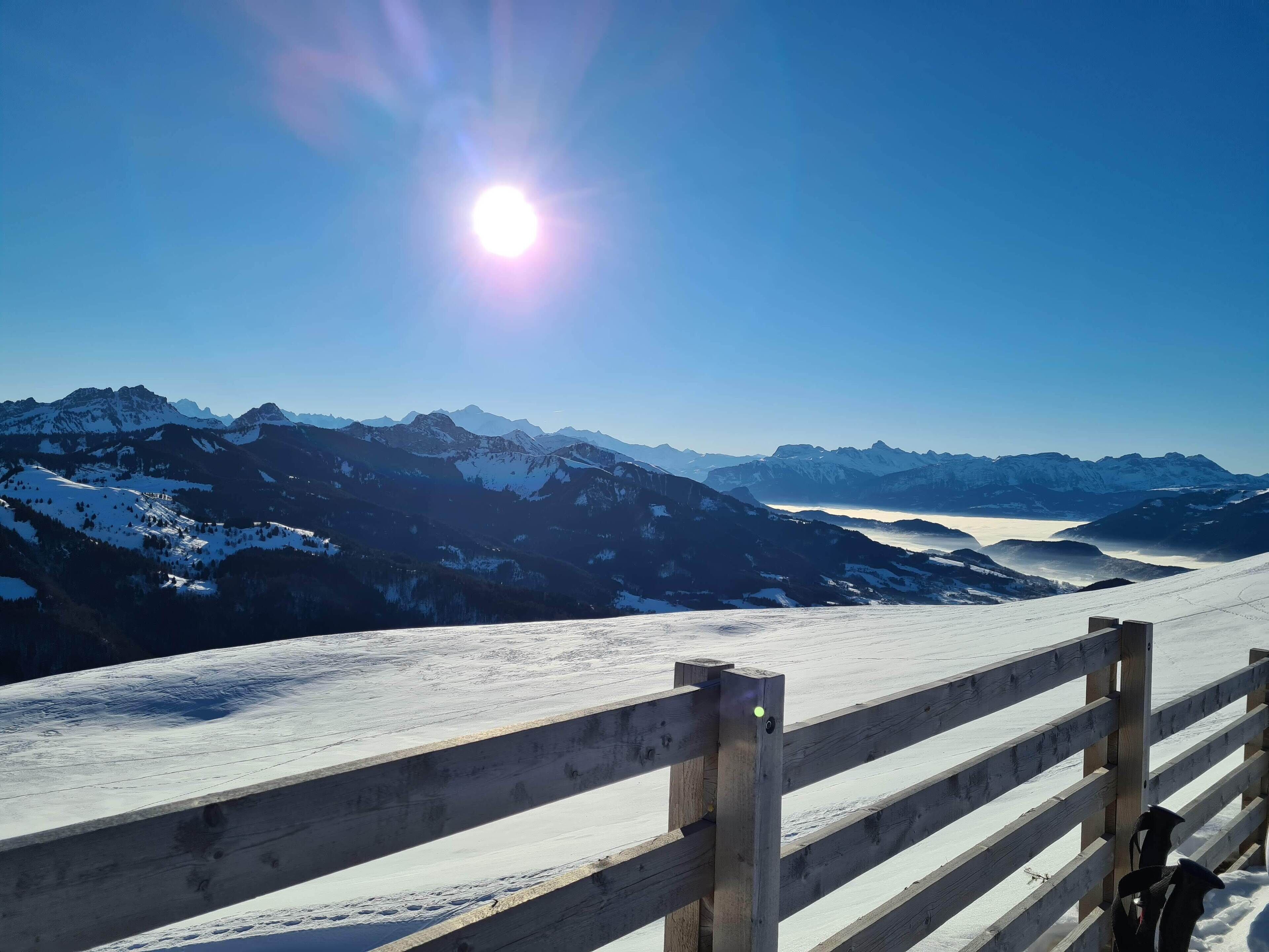 Cerca de madeira com vista para uma paisagem montanhosa coberta de neve e céu claro.