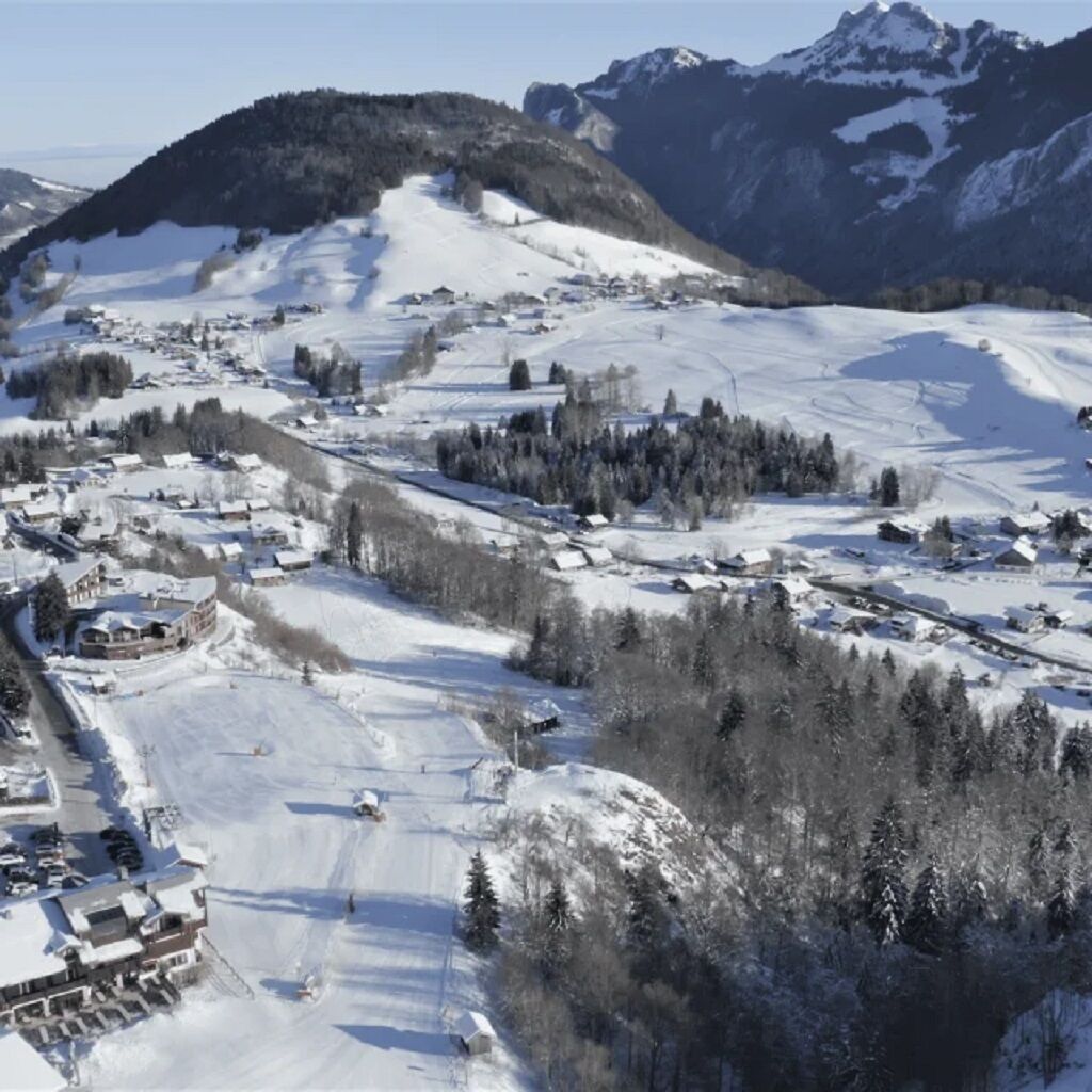 Ein verschneites Bergdorf mit Häusern und Skipisten.