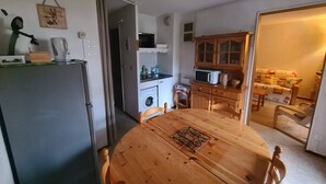 A compact kitchen with a refrigerator, microwave, and wooden cabinets. A dining table with chairs is in the center.