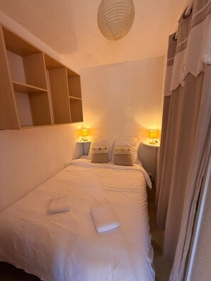 A bedroom with a bed, bedside lamps, a shelf, and a curtain.