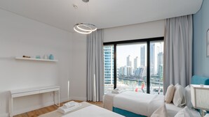 A modern hotel room with two beds, a desk, and a large window offering a city view. - Modern 3BR Maid s Iconic Ain Dubai Views (Dubai)