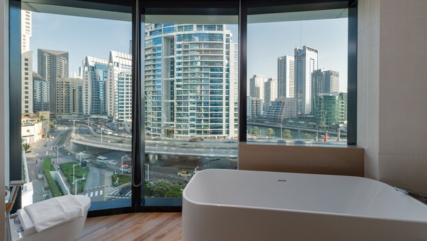 A modern bathroom with a large bathtub, a view of a cityscape through floor-to-ceiling windows, and a corner layout. - Modern 3BR Maid s Iconic Ain Dubai Views (Dubai)
