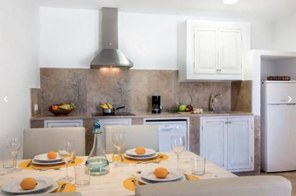 A modern kitchen with white cabinets, a stainless steel range hood, and a dining area set with orange placemats and wine glasses. - Ayurvila Wellness Retreat (Manacor)