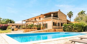 Una casa in pietra su due piani con piscina, immersa nel verde rigoglioso e palme.