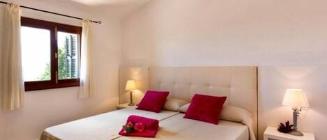 A hotel room with a bed, two pillows, a nightstand, a lamp, and a window with curtains.