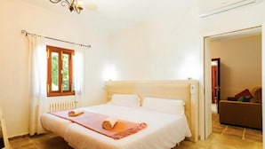 Een slaapkamer met een bed, een raam met gordijnen, een radiator en een deur die naar een andere kamer leidt.