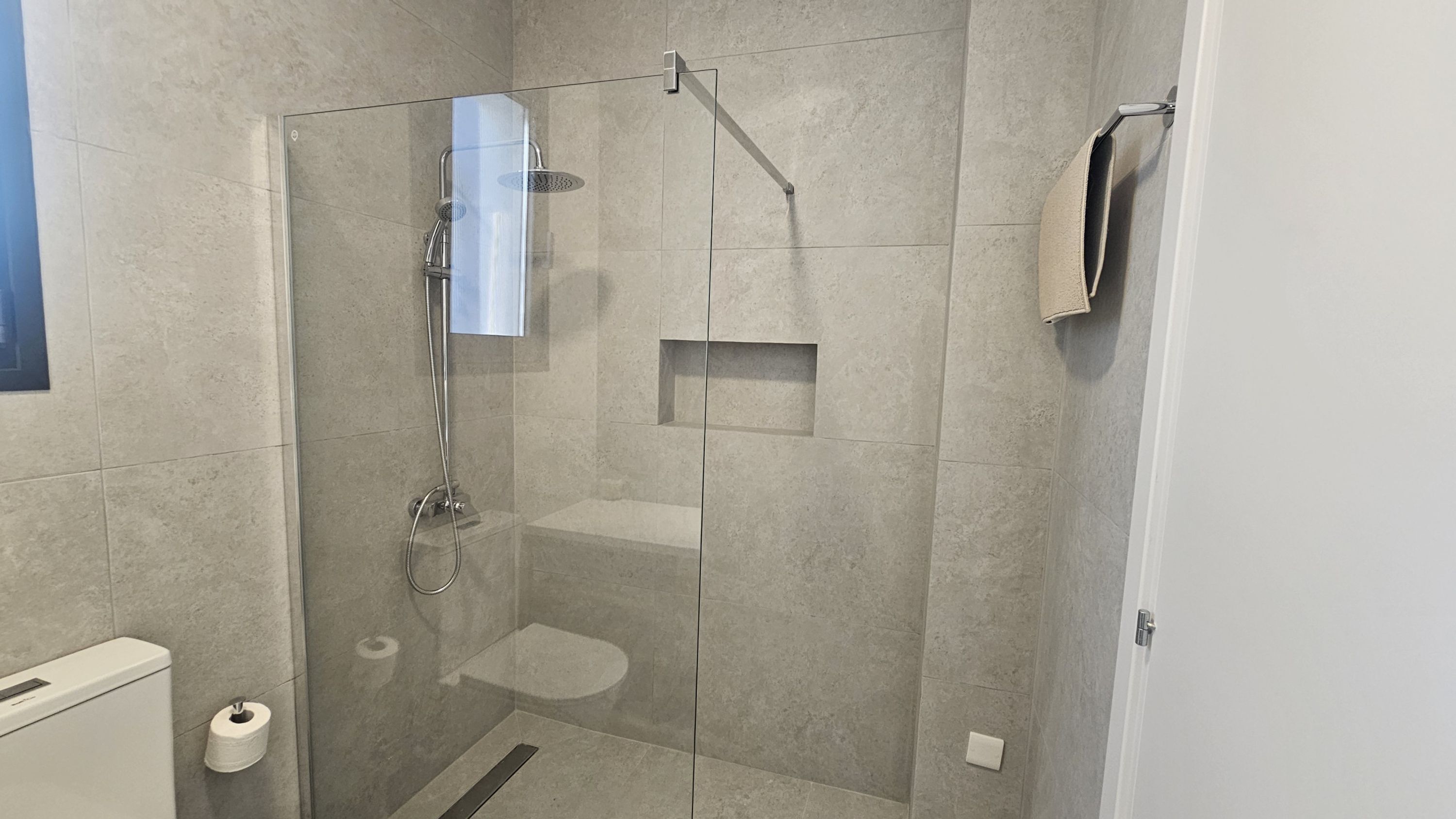 A modern bathroom with a glass-enclosed shower, a toilet, and a towel rack.